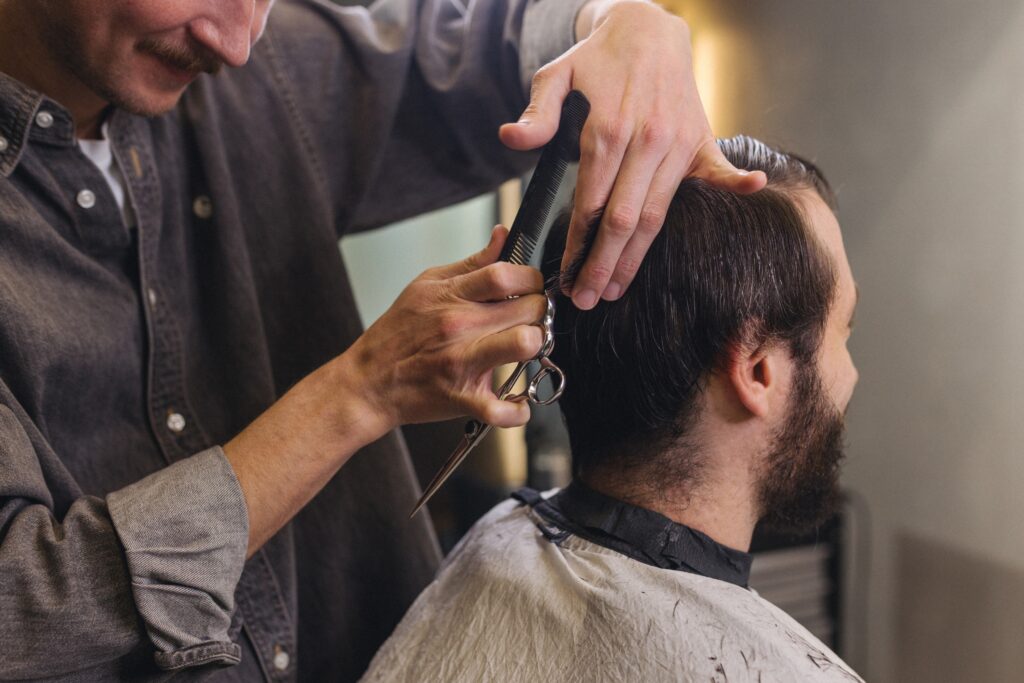 Professional barber using scissors and a comb during a men’s haircut