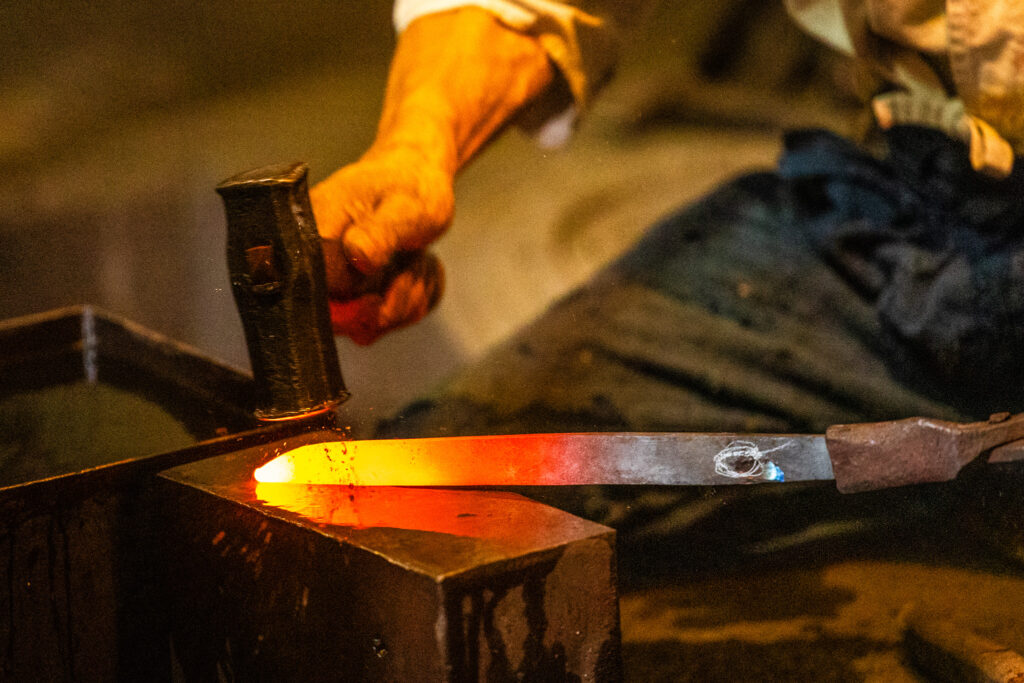 Close-up of a craftsperson hammering a heated steel blade on an anvil.