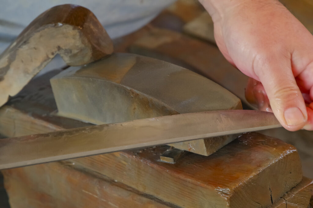 Close-up of a craftsperson polishing a sword blade on a wet sharpening stone.