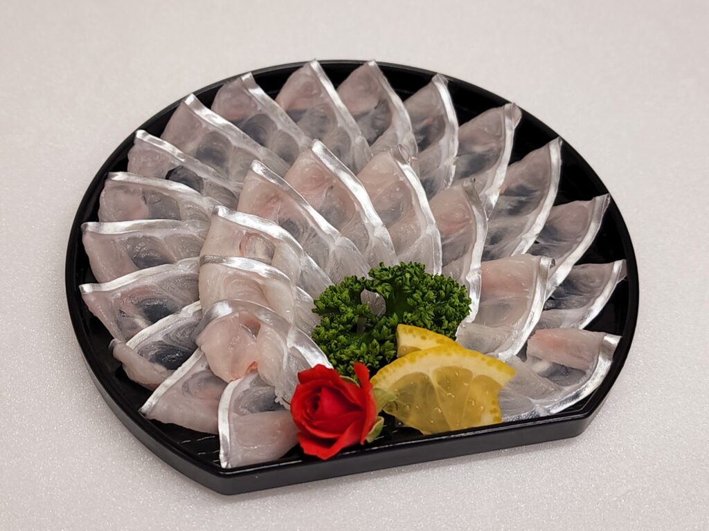 Thin slices of white fish sashimi arranged in overlapping rows on a black platter