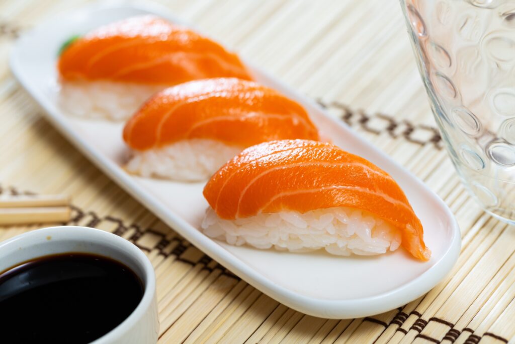 Three salmon nigiri sushi pieces arranged diagonally on a white plate