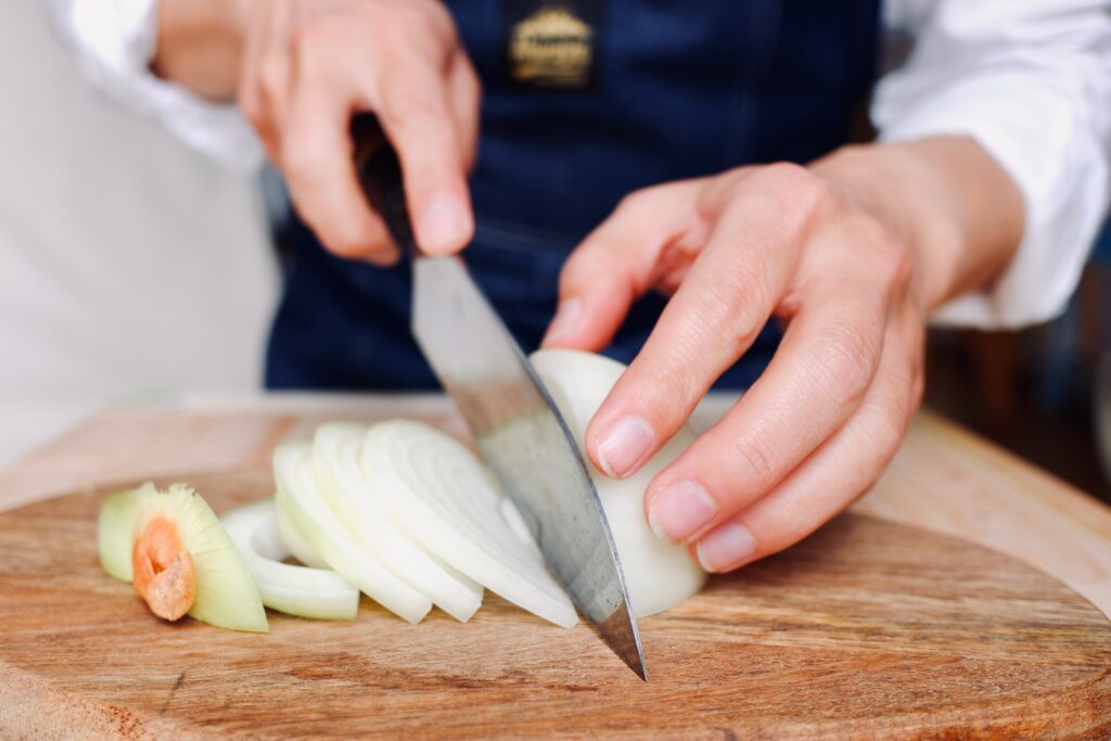 Hands slicing an onion with a kitchen knife on a wooden cutting board